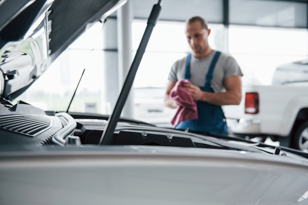 Gerichte foto. Man in blauw uniform werkt met kapotte auto. Reparaties maken