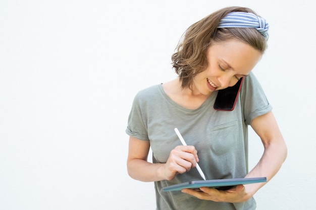 Gerichte glimlachende jonge vrouw die op het tabletscherm schrijven