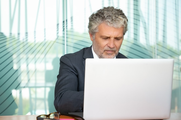 Gratis foto gerichte volwassen executive werken op de computer in kantoor, met behulp van witte laptop aan tafel. m.