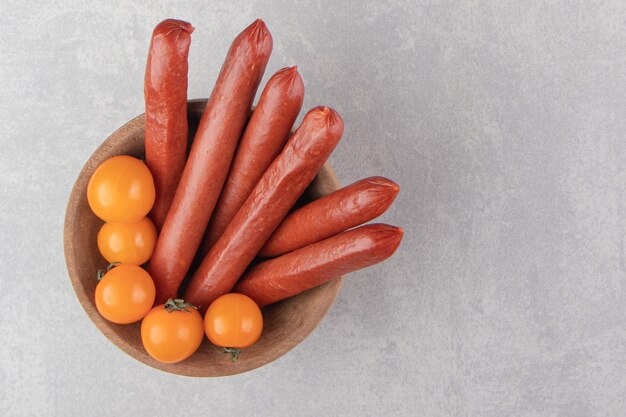 Gerookte worstjes en tomaten in houten kom.