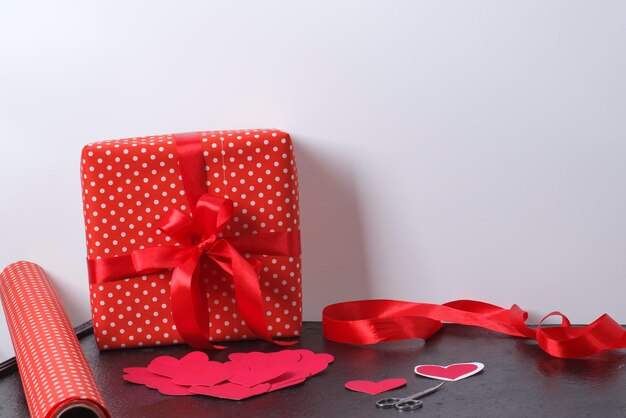 Geschenkdoos op tafel met rode papieren harten en linten op tafel tegen de muur. cadeautjes voorbereiden voor valentijnsdag