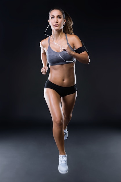 Geschikte en sportieve jonge vrouw die over zwarte achtergrond loopt.