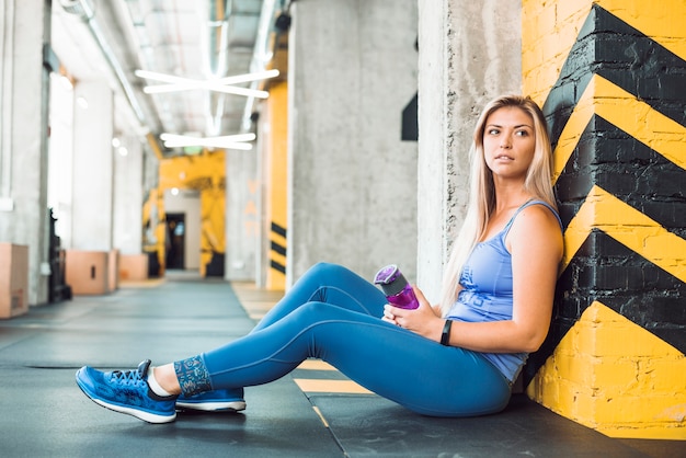 Geschikte vrouw met waterfles die op kolom in gymnastiek leunt