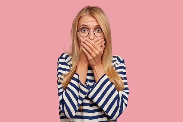 geschokt blonde vrouw poseren tegen de roze muur
