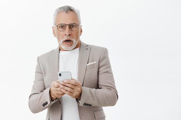 Geschokt hijgend senior man op zoek, met behulp van smartphone