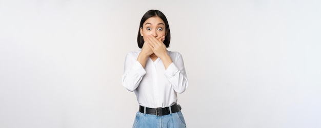 Geschokt jong Aziatisch meisje sluit mondbedek lippen met handen en kijkt verbaasd over een witte achtergrond Taboe-gebaar