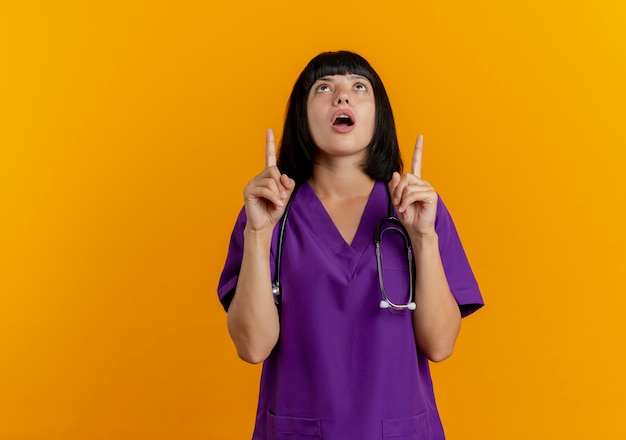 Geschokt jonge brunette vrouwelijke arts in uniform met stethoscoop
