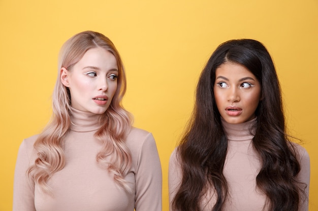 Geschokt jonge twee dames permanent over gele muur