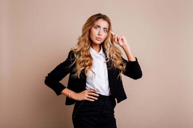 Geschokt jonge zakenvrouw of werknemer in stijlvolle pak poseren over beige muur.