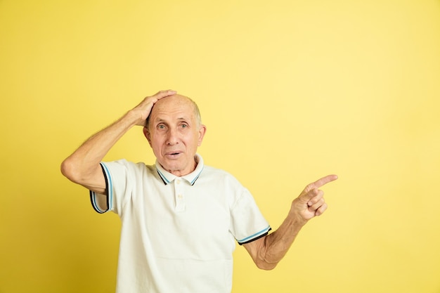 Geschokt, naar de zijkant wijzend. Portret van een blanke senior man op gele studio achtergrond. Mooi mannelijk emotioneel model. Concept van menselijke emoties, gezichtsuitdrukking, verkoop, welzijn, advertentie. Copyspace.