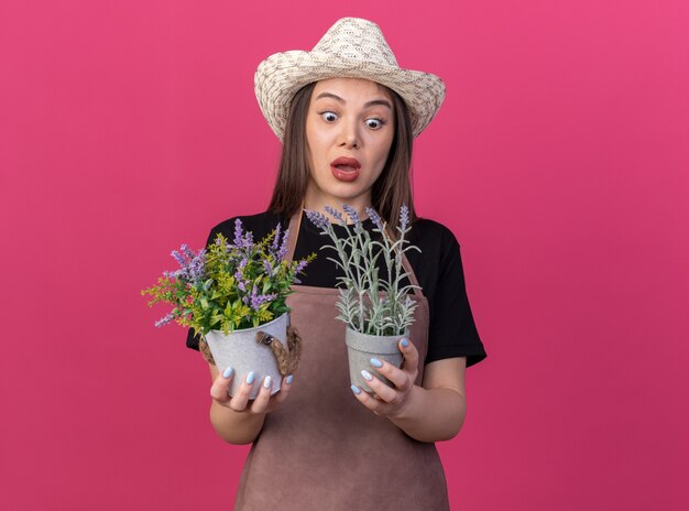 Geschokt vrij Kaukasische vrouwelijke tuinman tuinieren hoed dragen en kijken naar bloempotten op roze