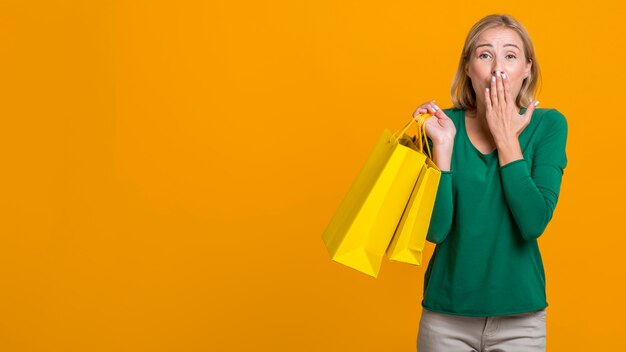 Geschokt vrouw die haar mond bedekt terwijl ze veel boodschappentassen vasthoudt met kopie ruimte