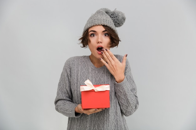 Geschokt vrouw gekleed in trui en warme muts bedrijf cadeau.