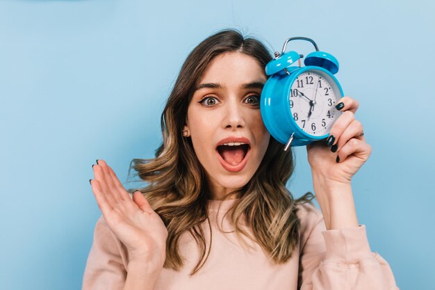 Geschokt vrouw poseren met open mond in de ochtend Studio shot van mooi krullend meisje met klok