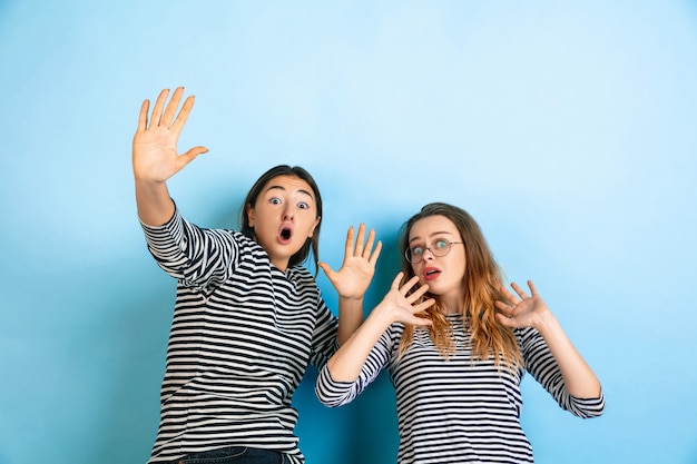 Geschokte en bange jonge emotionele vrouwen die op de muur van de gradiënt blauwe studio worden geïsoleerd