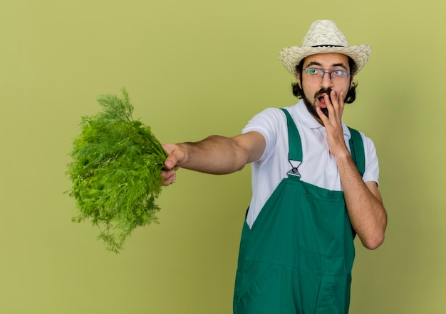 Gratis foto geschokte mannelijke tuinman in optische bril met tuinhoed legt hand op mond