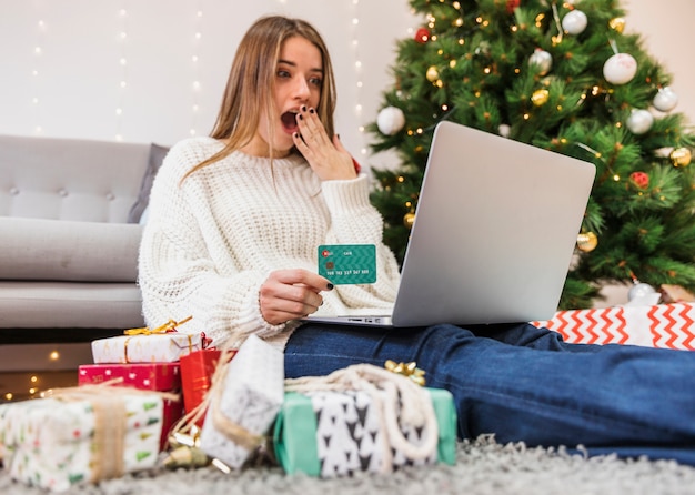 Geschokte vrouw die online bij Kerstboom winkelt