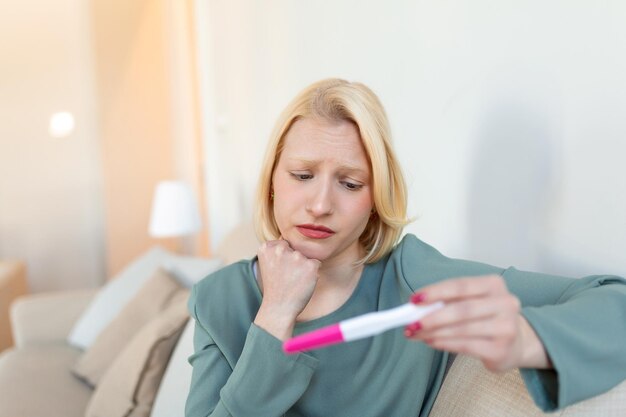 Geschokte vrouw kijkt naar controlelijn op zwangerschapstest Alleenstaande trieste vrouw klaagt met een zwangerschapstest Depressieve vrouw met negatieve zwangerschapstest