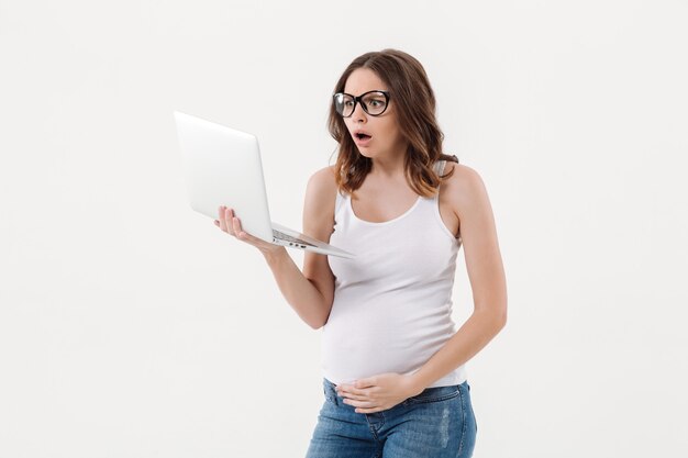 Geschokte zwangere vrouw die laptop computer met behulp van.