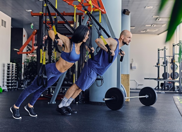 Geschoren hoofd atletische man en slanke brunette vrouw oefenen met trx bandjes in een sportschool club.
