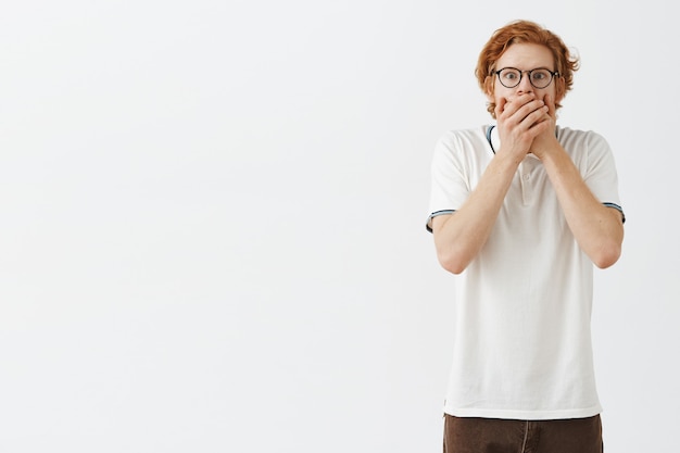 Gratis foto geschrokken bebaarde roodharige man poseren tegen de witte muur met een bril