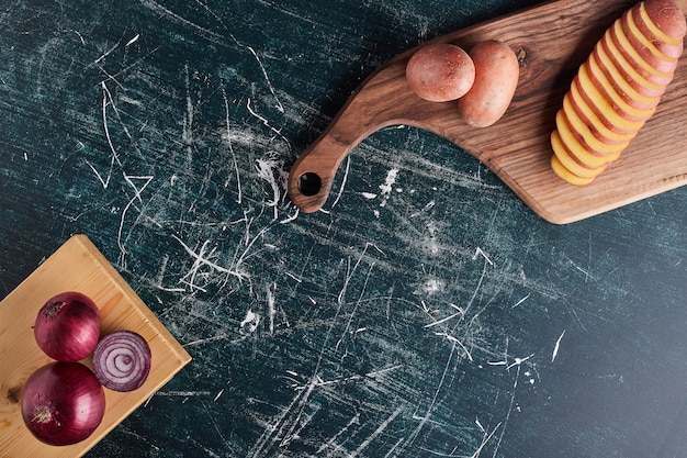 Gratis foto gesneden aardappel en rode uien op een houten bord.