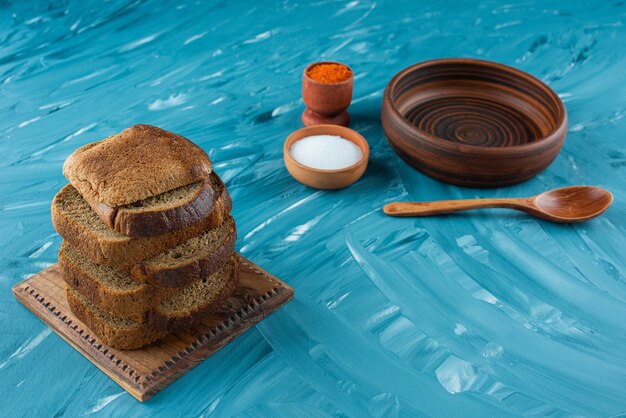 Gratis foto gesneden bruin brood met zout en een lege houten lepel op een blauwe achtergrond.