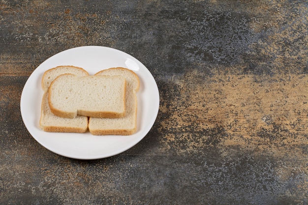 Gesneden bruin brood op witte plaat.