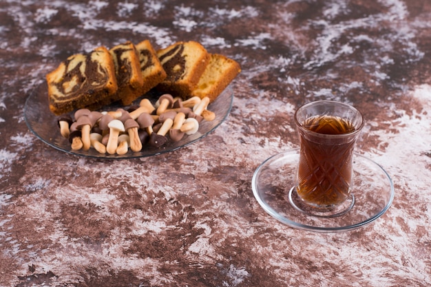 Gesneden cacaotaart met koekjes in een glazen schotel met een glas thee