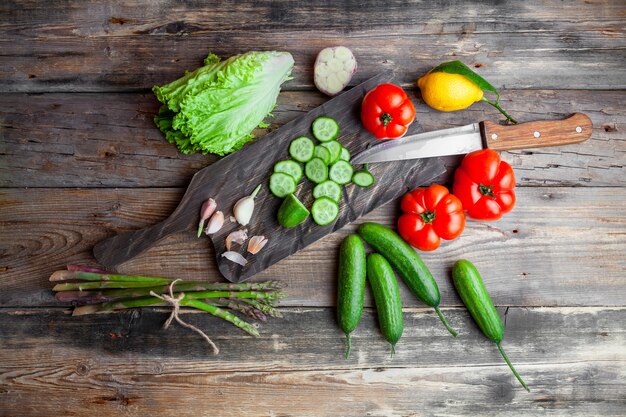 Gesneden komkommer in een snijplank met tomaten, sla, citroen bovenaanzicht op een donkere houten achtergrond