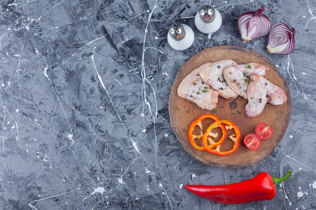 Gesneden paprika, tomaten en vleugel op een bord naast ui, zout en peper op het blauwe oppervlak