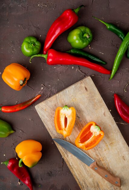 gesneden peper op snijplank met mes en paprika's rond op kastanjebruine tafel