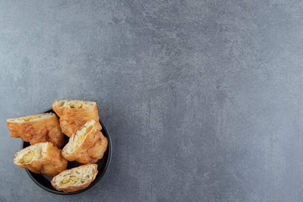 Gesneden piroshki met aardappelen in zwarte kom.