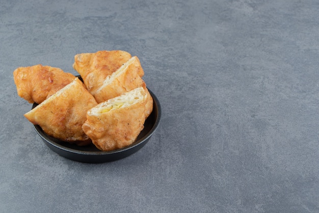 Gesneden piroshki met aardappelen in zwarte kom.