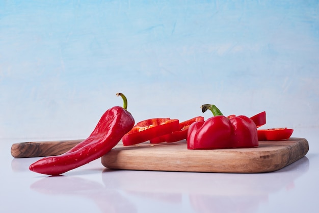 Gratis foto gesneden rode chili en paprika op een houten schotel op blauw.