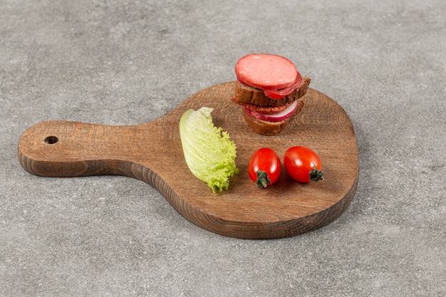 Gesneden salami met roggebrood en tomaat op een houten bord.