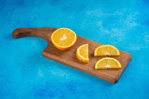 Gesneden sinaasappel op een houten bord op blauw.
