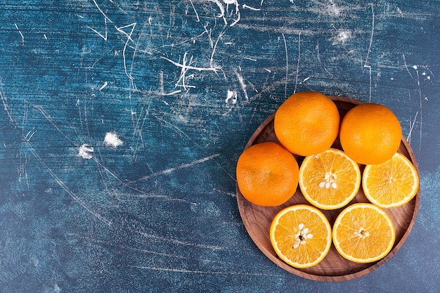 Gesneden sinaasappelen en mandarijnen op een houten schotel op blauwe achtergrond. Hoge kwaliteit foto