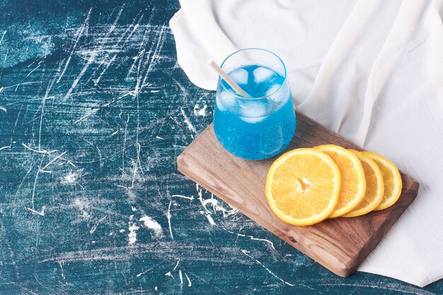 Gesneden sinaasappelen met een kopje drank op blauw.