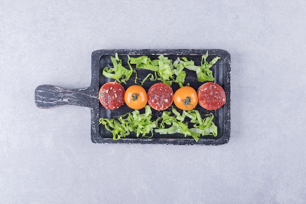 Gesneden smakelijke worstjes met ketchup en tomaten op zwart bord.