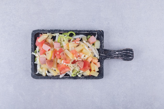 Gesneden smakelijke worstjes met verse salade op zwart bord.