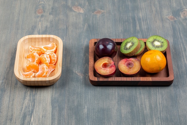 Gesneden verse kiwi met sinaasappel en pruimen op een houten bord