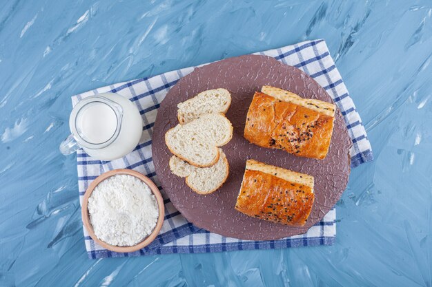 Gesneden witbrood met een glazen kruik melk en een houten kom met bloem.