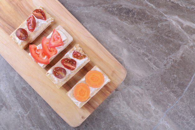 Gesneden wortelen en tomaten op knapperige broden, op het marmeren oppervlak