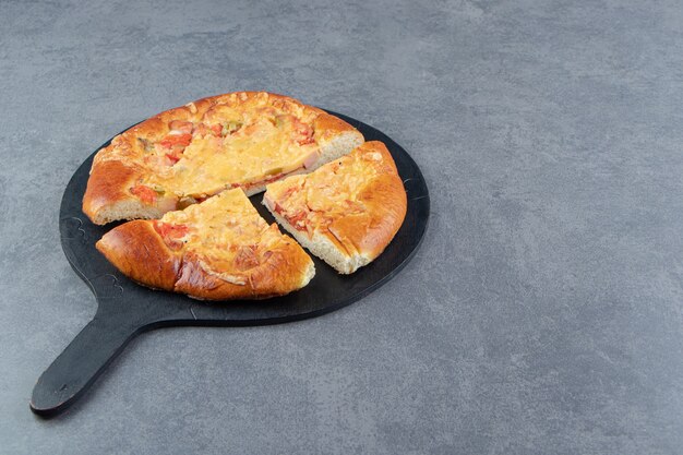 Gesneden zelfgemaakte pizza op zwarte snijplank.