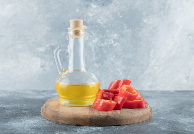Gesneden zoete paprika met een glazen fles olie op een houten bord.