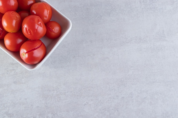 Gesneden zoute tomaten in houten kom die op steenachtergrond wordt geplaatst.