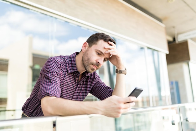 Gespannen man leest verontrustend nieuws op smartphone terwijl hij op de reling in het winkelcentrum leunt