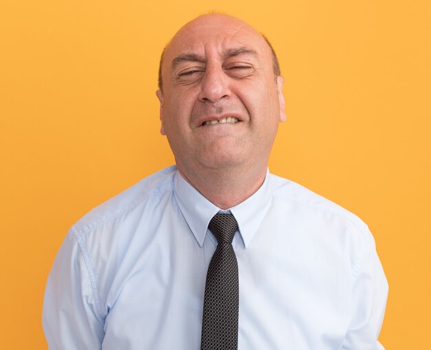 Gespannen met gesloten ogen man van middelbare leeftijd met wit t-shirt met stropdas geïsoleerd op oranje muur