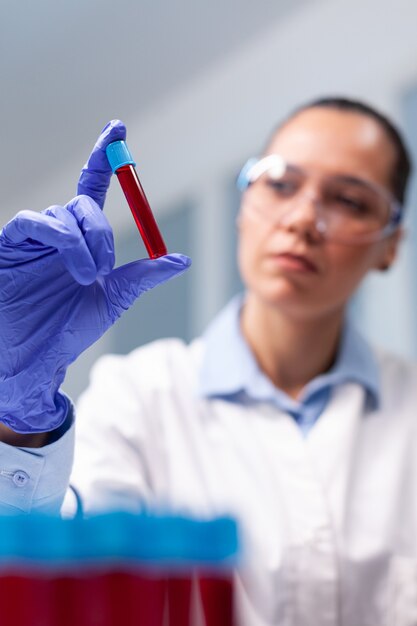 Gespecialiseerde vrouwelijke arts kijkt naar klinische vacutainer dna-bloed die biologie-expertise analyseert